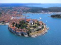 Rovinj, położone w Chorwacji na słonecznym półwyspie Istria urokliwe miasteczko portowe, jest jednym z najbardziej znanych kurortów wczasowych w tym regionie. Romantyczne krajobrazy, lazurowe i krystalicznie czyste lustro Morza Adriatyckiego, w którym odbija się wenecka architektura sprawiają, że Rovinj to miejsce szczególnie ukochane przez artystów, malarzy i aktorów. Wielu z nich wybrało je na swoje miejsce zamieszkania, dzięki czemu miasto zyskało z czasem przydomek ”chorwackiego Saint Tropez”, a jego ulice zapełniły się malarskimi i fotograficznymi pracowniami. 

”Jeśli zanurzysz palec w morzu, łączysz się z całym światem” (Kad stavis prst u more, povezan si scijelim svijetom) - brzmi dalmatyńskie przysłowie mieszkańców wysp Adriatyku. O mocy tej starej mądrości ludowej przekonują się turyści, którzy w wakacyjnej porze spędzają wczasy w nadmorskich miastach Chorwacji. Słoneczny klimat, morze, plaże, luksusowe apartamenty, wyjątkowa gościnność i otwartość mieszkańców sprawiają, że wypoczynek w chorwackich kurortach cieszy się od lat ogromną popularnością.


Pogoda, klimat i lokalizacja


Rovinj leży na zachodnim wybrzeżu półwyspu Istria, zajmując obszar 80 km2. Panuje tu ciepły klimat śródziemnomorski, ze średnią temperaturą 16°C i subtropikalną roślinnością. W ciągu roku przez około 2400 godzin świeci słońce, od połowy maja do połowy sierpnia można liczyć na ponad 10 godzin światła słonecznego dziennie. Zimy są łagodne, a lato bardzo ciepłe. W lipcu średnia temperatura wynosi 22,3°C. Od połowy czerwca do połowy września temperatura morza przekracza 20°C. Znajdują się tutaj parki krajobrazowe i pomniki przyrody: wyspy wchodzące w skład Archipelagu Rovinj, Jaskinia Romualda, mokradło Palud, kamieniołom ”Cave di Monfiorenzo”.


Historia


Rovinj w czasach starożytnych był wyspą zamieszkaną już w VII w. p. n. e. przez lud Ilirów, który na przełomie II i I wieku p. n. e. został podbity przez Rzymian i włączony w skład prowincji Iliria. Miasto posiada burzliwą historię, wielokrotnie przechodziło pod panowanie kolejnych władców. Na przestrzeni wieków było częścią Bizancjum, Imperium Frankońskiego oraz Republiki Wenecji (XIII - XVIII w.), kiedy w 1531 roku zyskało prawa miejskie. Z tego właśnie okresu pochodzą zabytkowe fortyfikacje, mury i bramy (najbardziej znana to ”Łuk Balbi” z 1680 roku) i inne przykłady weneckiej architektury. Aż do połowy XVIII w. Rovinj był miastem na wyspie. Cieśnina oddzielającą wyspę od stałego lądu została zasypana dopiero w 1763 roku. Okres świetności Rovinj przypada na okres panowania Habsburgów (1813-1920), kiedy to stało się największym miastem na zachodnim wybrzeżu Istrii. 


Zabytki, Stare Miasto


Miasto odznacza się zróżnicowaną architekturą, będącą mieszanką zabytkowych pozostałości Republiki Wenecji, oraz urokliwego budownictwa śródziemnomorskiego, z charakterystycznymi, malowniczymi domkami o czerwonych dachach. Pozostałe dziś mury miejskie, brama miejska zwana ”Łuk Balbi” (z 1680 roku) i późno-renesansowa wieża zegarowa, zaliczane do najbardziej atrakcyjnych obiektów turystycznych, są datowane na okres wenecki. Zabytkowe kamienice i renesansowe pałace znajdujące się na terenie całego miasta przypominają o jego historycznej świetności. To właśnie w Rovinj znajduje się największa świątynia w całej Istrii - umiejscowiona na wzgórzu, pochodząca z połowy XVIII w. Katedra Św. Eufemii. Tam, wspiąwszy się na 57-metrową wieżę wznoszącą się nad katedrą, spragnieni wrażeń turyści podziwiają z zapartym tchem urzekający widok obejmujący całe wybrzeże, zabytkową architekturę miasta, plaże, luksusowe hotele i wyspy Archipelagu Rovinj. Po atrakcjach widokowych można poświęcić czas na łyk historii i zwiedzenie zabytkowego wnętrza katedry, gdzie w grobowcu za ołtarzem spoczywają szczątki św. Eufemii. 


Wycieczki, rejsy, festiwale, atrakcje


Po spacerze przez historyczną część naszego miasta, przychodzi czas na wycieczki i miejscowe atrakcje, wobec których nie sposób pozostać obojętnym. Pamiętając o portowym charakterze miasta odkrywamy, że z przystani odpływają promy do samej Wenecji, a także statki turystyczne, które oferują morską przygodę połączoną z eksploracją wysp Archipelagu Rovinj (z których część nadal jest dziewicza). Turyści pozostający w żeglarskim nastroju, mogą zajrzeć do oceanarium pełnego barwnej, morskiej flory i fauny. Lato w Rovinj upływa pod znakiem festiwali, z których najważniejszym jest wakacyjne, trwające od lipca do września ”Rovinjsko lieto”, gwarantujące niezapomniane fiesty pod otwartym niebem. Amatorzy sportu znajdą tu okazję, by spróbować żeglarstwa, nurkowania, nart wodnych, windsurfingu, lub bardziej ekstremalnej przygody, jaką jest wspinaczka na nadmorskich skałach, gdzie po zastrzyku adrenaliny można przespacerować się brzegiem plaży, lub zażyć ożywczej kąpieli w morzu. 


Kuchnia, kulinaria


Specjalnością lokalną są tu zdecydowanie śródziemnomorskie, wydobyte wprost z Adriatyku frutti di mare, których dostarcza najstarsza w kraju przetwórnia ryb. Warto również odwiedzić lokalne place targowe, gdzie w gwarnej atmosferze mieszkańcy handlują miejscowymi specjałami: oliwą, soczystymi brzoskwiniami i wieńcami kolorowych papryk. Wielbicieli wina z pewnością zaspokoją pochodzące z lokalnych winnic gatunki o głębokim aromacie - Burgonjac i Malvazija. Będąc w tym rejonie należy skosztować istryjski pršut (wędzoną szynkę), do której zazwyczaj podaje się owczy ser, oraz dania o nazwie maneštra - zupę przygotowywaną z różnego rodzaju warzyw.


Noclegi, zakwaterowanie, hotele, apartamenty


Rovinj posiada szeroką ofertę noclegową. Znajdują się tutaj hotele o każdym standardzie, luksusowe apartamenty, prywatne kwatery, kempingi i domki wakacyjne. Każdy turysta znajdzie tu odpowiednią dla swojej kieszeni opcję noclegową.
